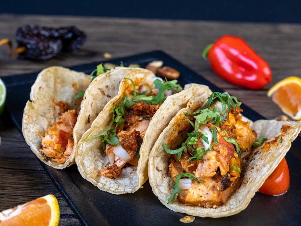 Three al pastor tacos on a slate board